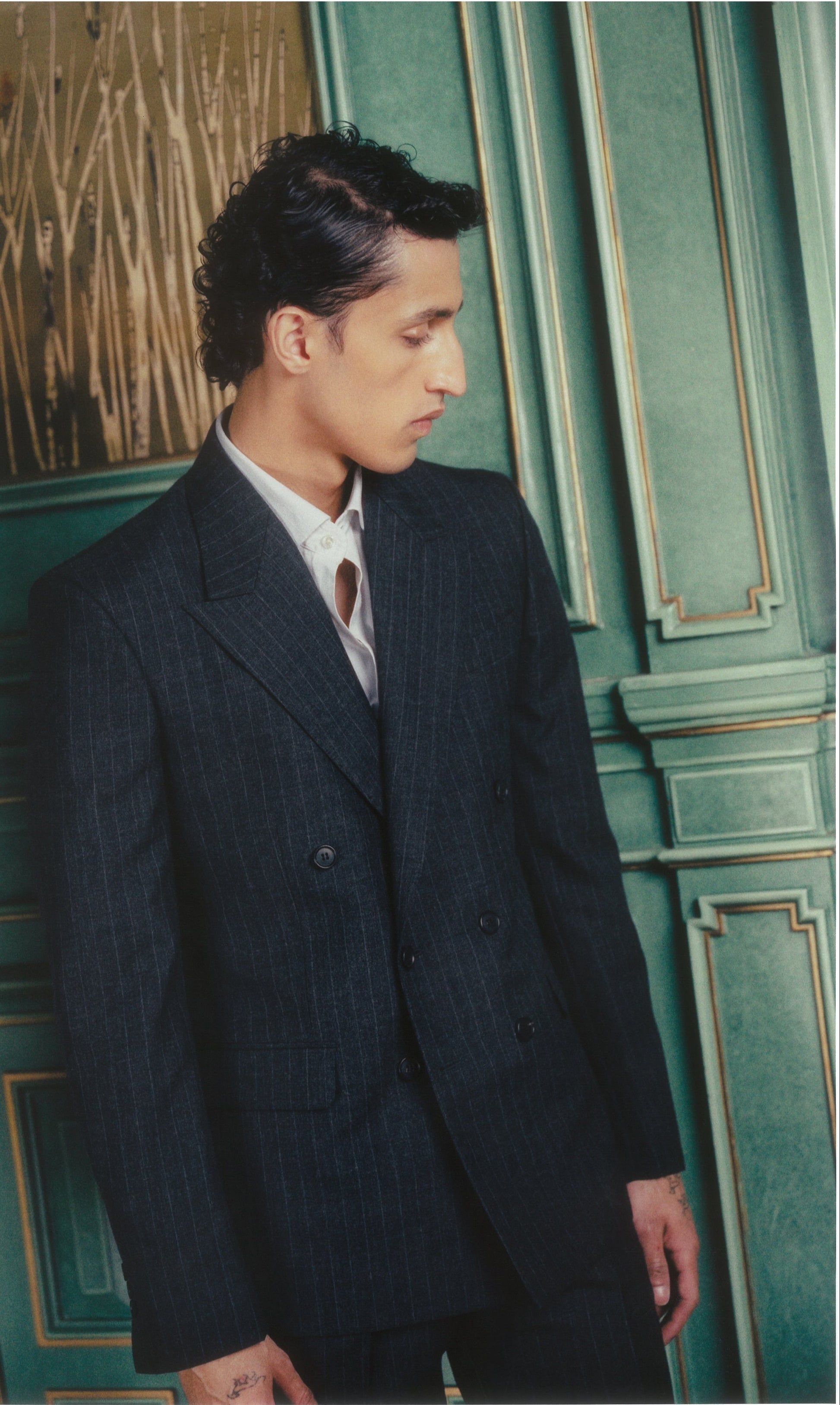 Man in a dark suit standing against a green wall with decorative elements