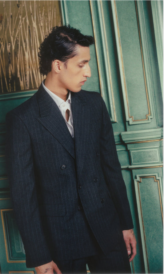 Man in a dark suit standing against a green wall with decorative elements
